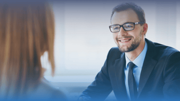 White man with glasses in a suit smiling during an interview