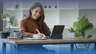 Asian woman watching webinar and taking notes.