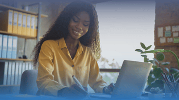 African American woman takes notes while watching virtual panel event on laptop.