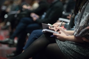 Conference style seating with multiple people sitting and writing notes during a talk